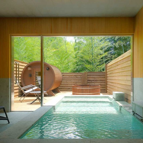 静岡県熱海市のアウトドアホテル「THE BASE GLAMPING ATAMI PREMIER」に導入されたバレルサウナ BURROW mini2 とヒノキ浴槽。竹林に面したテラスから室内の温泉を望む